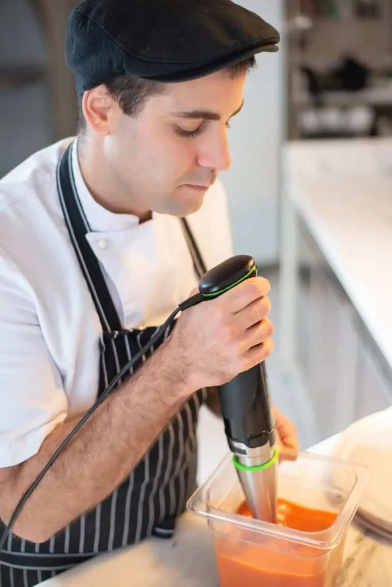 Chef blending soup with immersion blender, showcasing culinary skills in a modern kitchen.